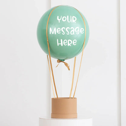 Personalized eucalyptus green hot air balloon decoration with custom message, gold ribbons, and cardboard basket
