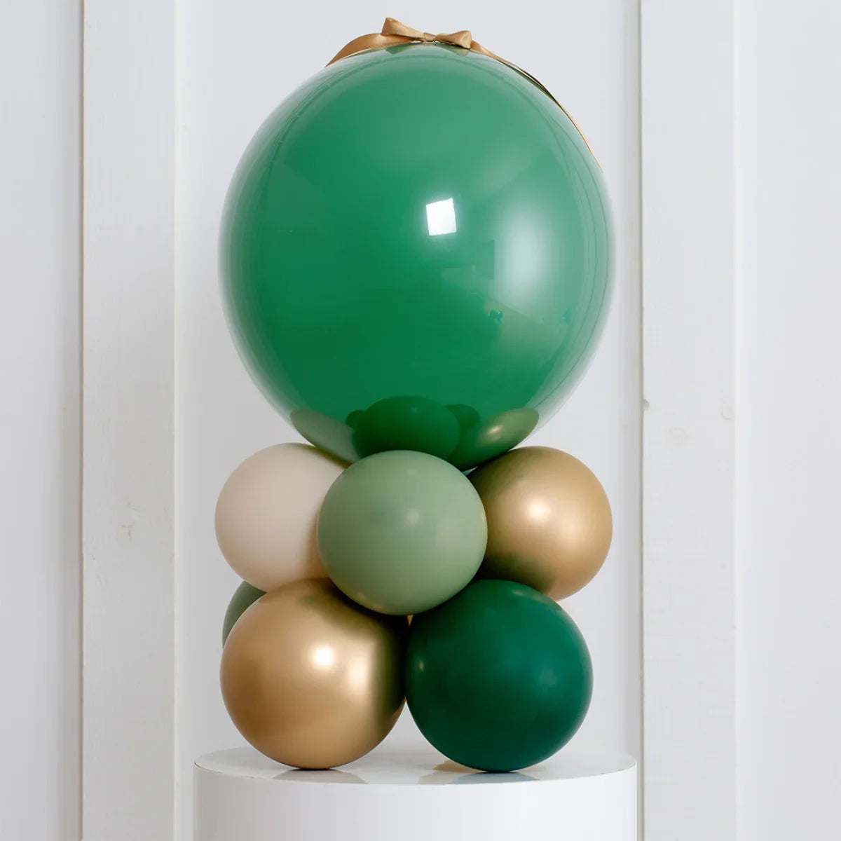 Forest green and gold air-filled balloon stack decoration on white pedestal