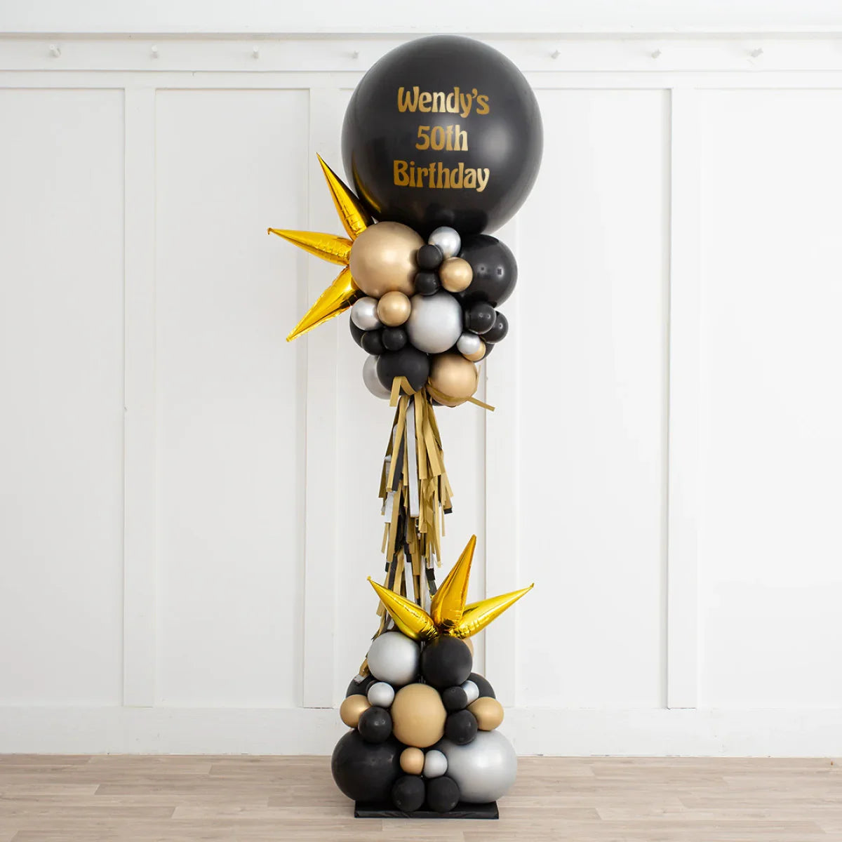 Black, gold, and silver balloon arrangement with gold spikes and text 'Wendy's 50th Birthday' for party decoration