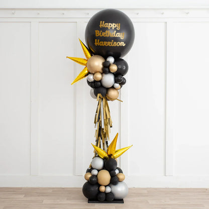 Black, gold, and silver birthday balloon arrangement with 'Happy Birthday Harrison' text in a white room