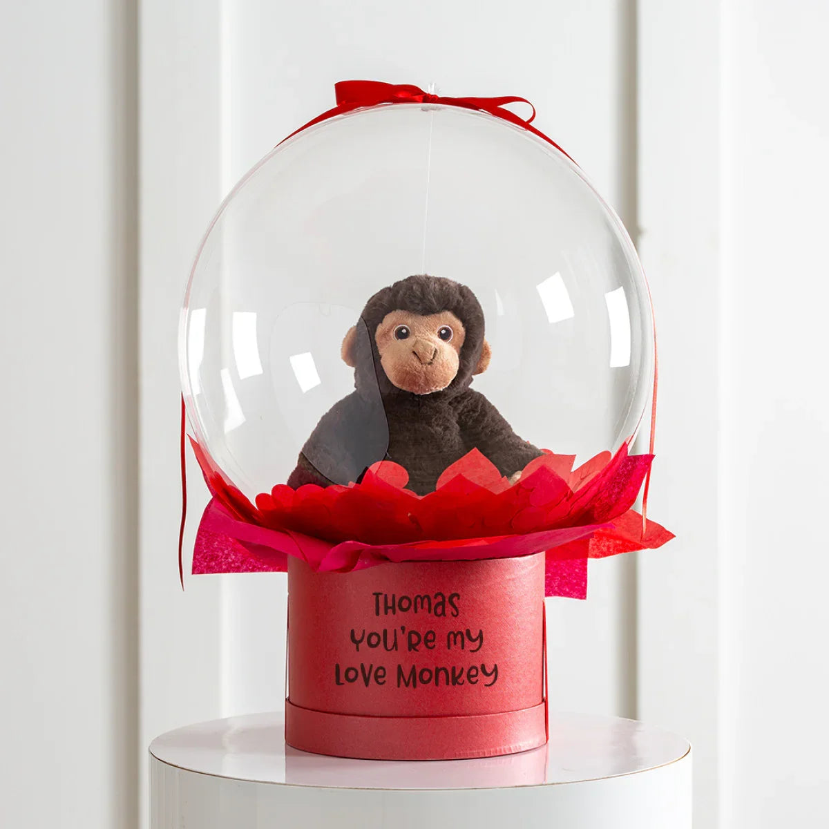 Plush monkey inside clear bubble with red base and tissue, personalized message reading 'Thomas You're my Love Monkey'