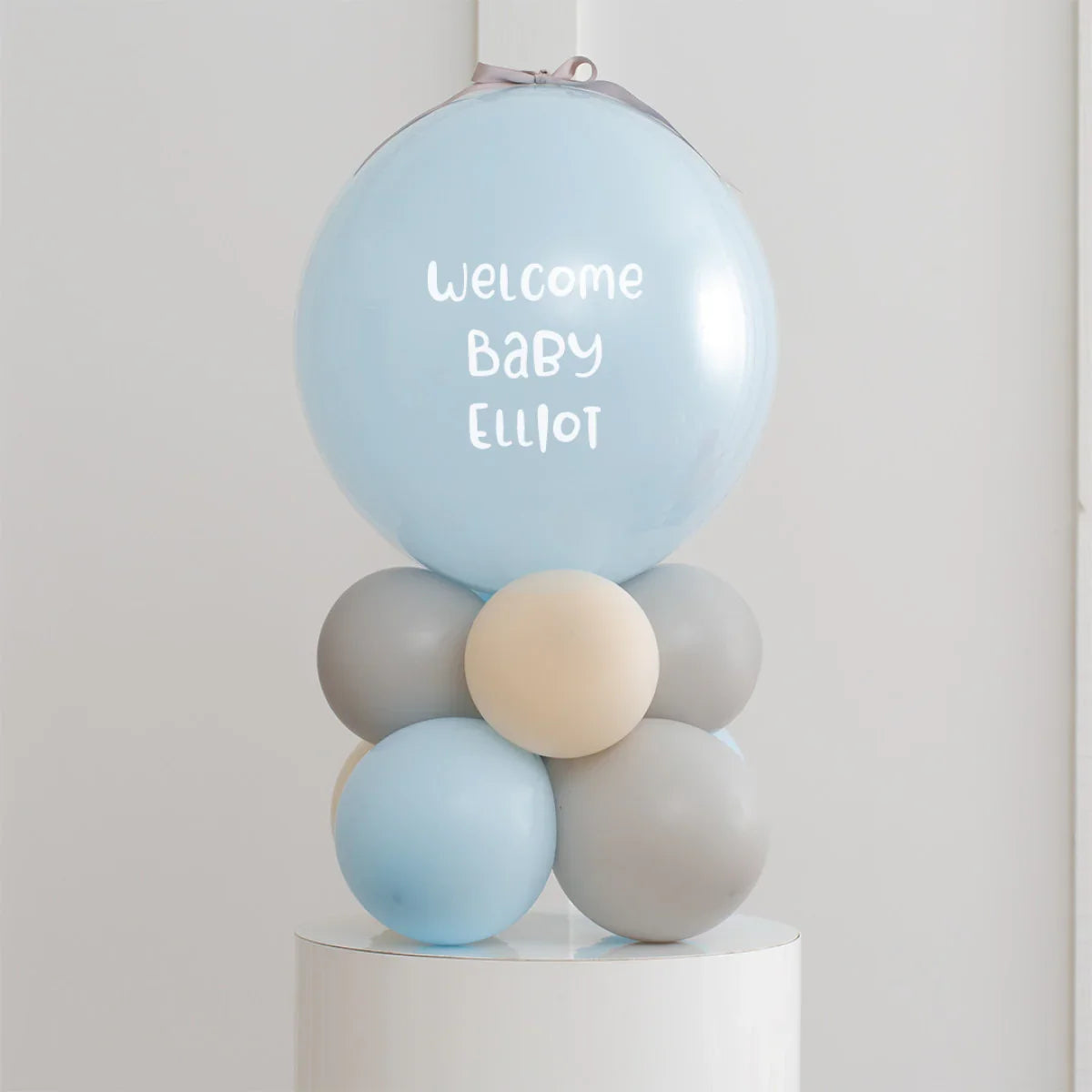 Personalised blue baby welcome balloon with gray and cream smaller balloons on white pedestal