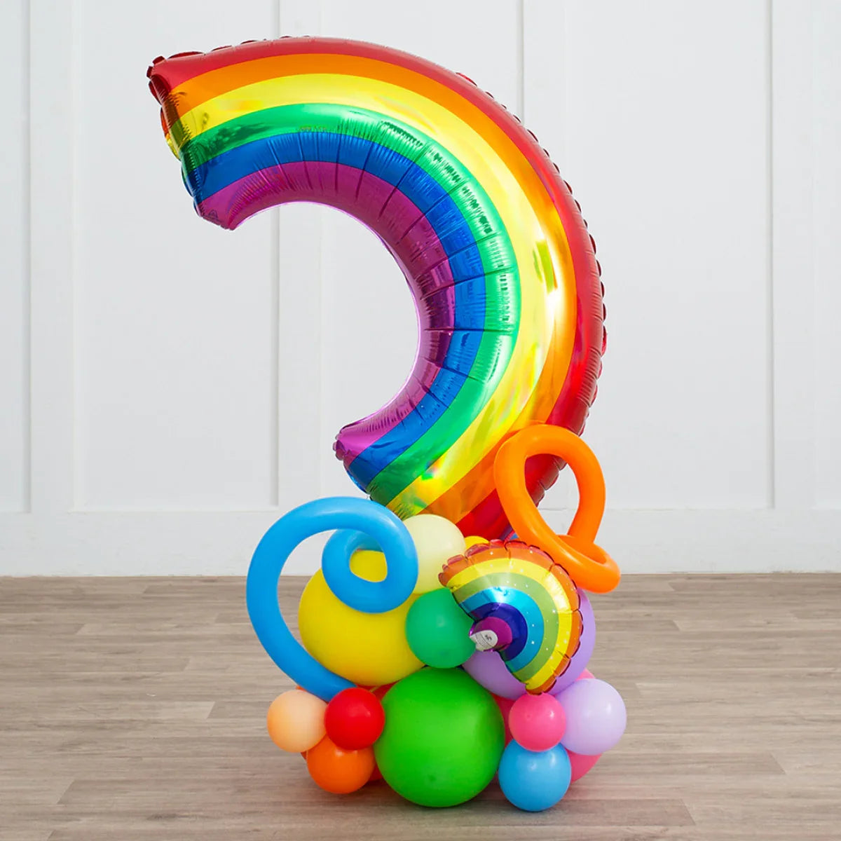 Colorful rainbow foil balloon centerpiece with assorted bright latex balloons on wooden floor