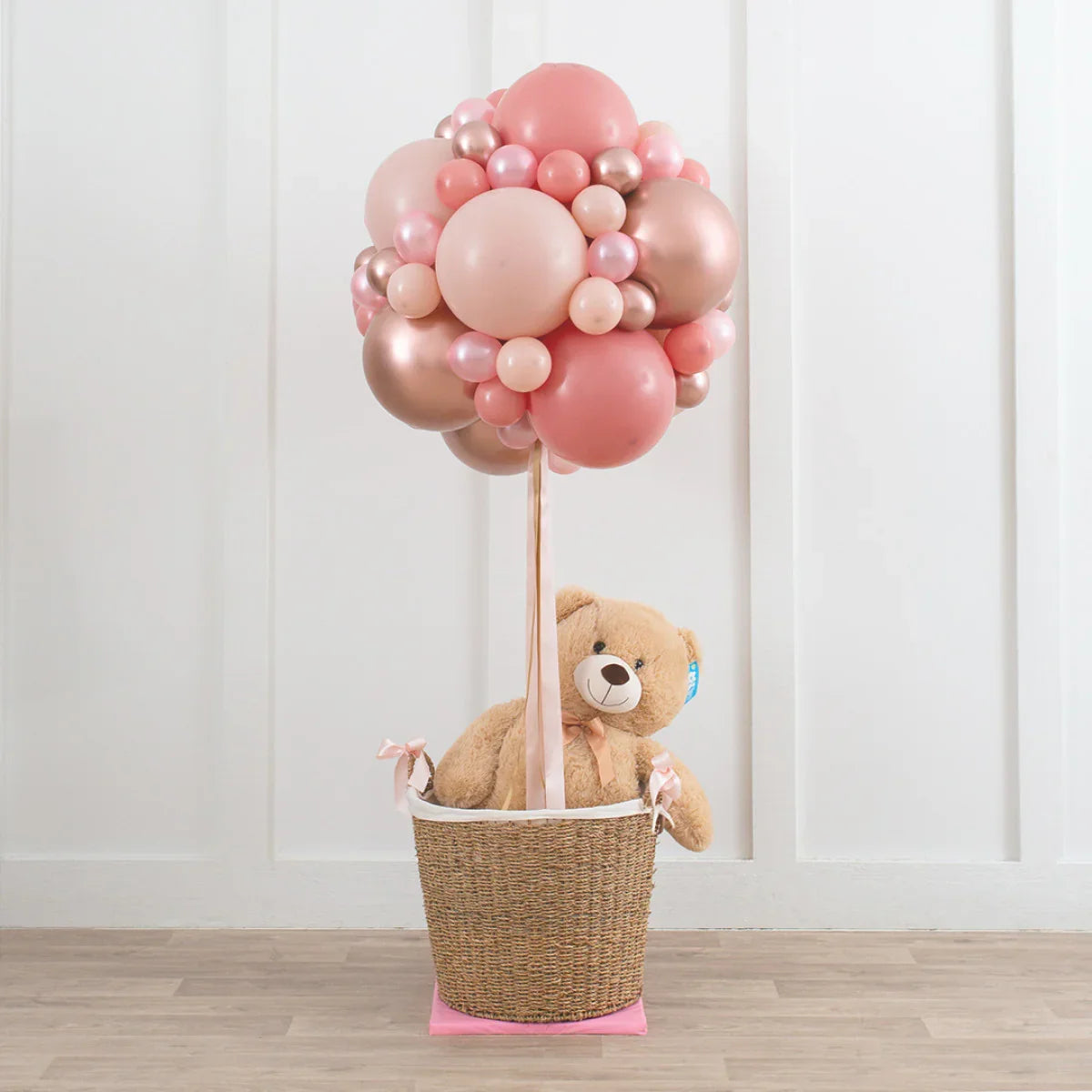 Rose gold blush balloon arrangement shaped like a hot air balloon with teddy bear in woven basket