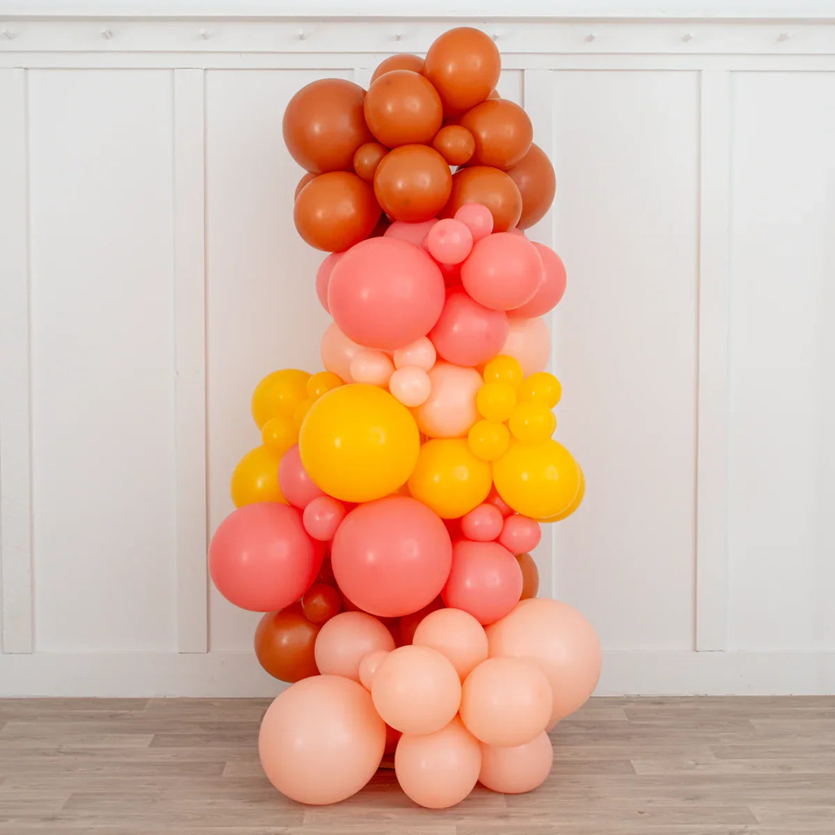 Tropical sunset balloon pillar in warm shades of orange, pink, and yellow on wood floor