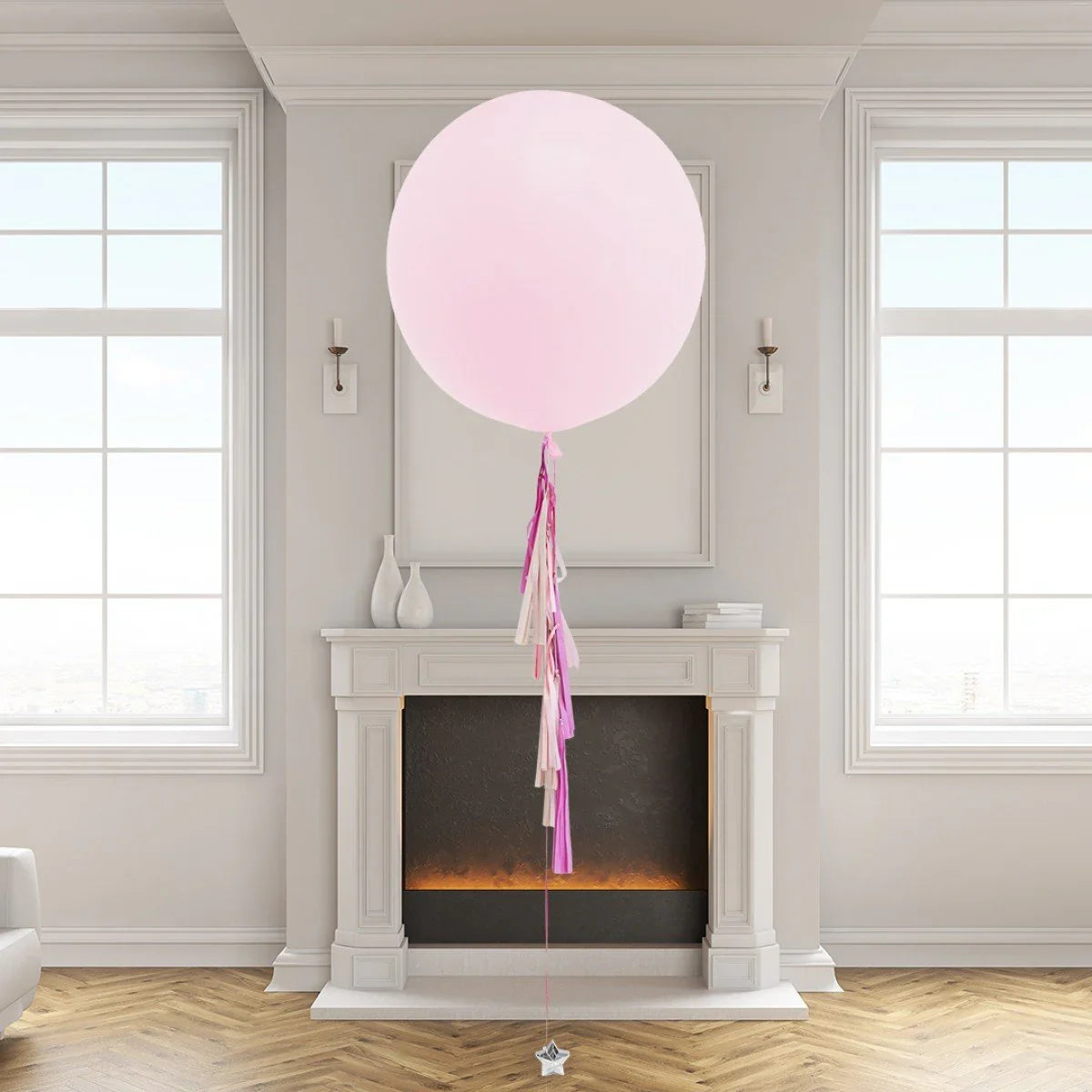 Large pastel pink balloon with pink and white tassels floating in elegant room with mantle and windows