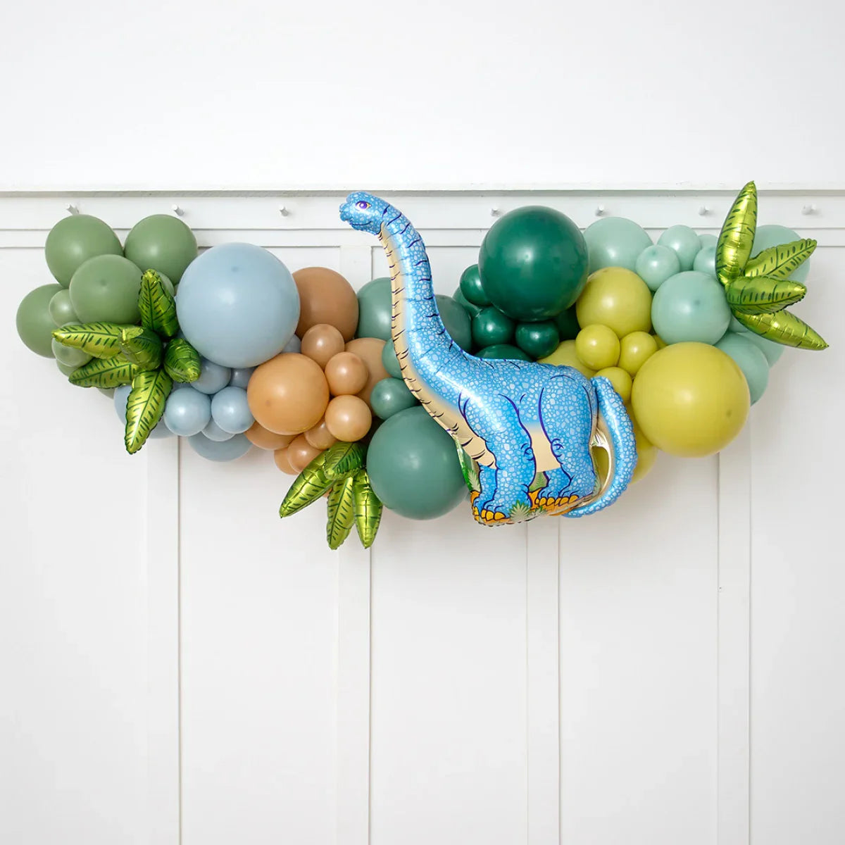 Colorful balloon garland with green leaf balloons and a blue dinosaur foil balloon on white wall